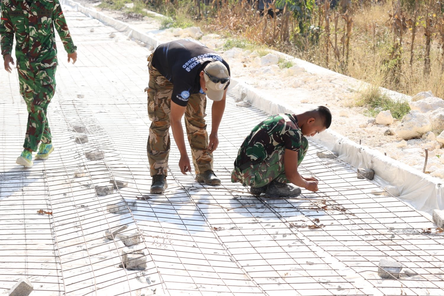 Ketelitian prajurit Satgas TMMD ke 129 dalam bahu-membahu memasang batu penahan di bawah rangkaian besi wiremesh sebelum tahap pengecoran jalan dimulai
